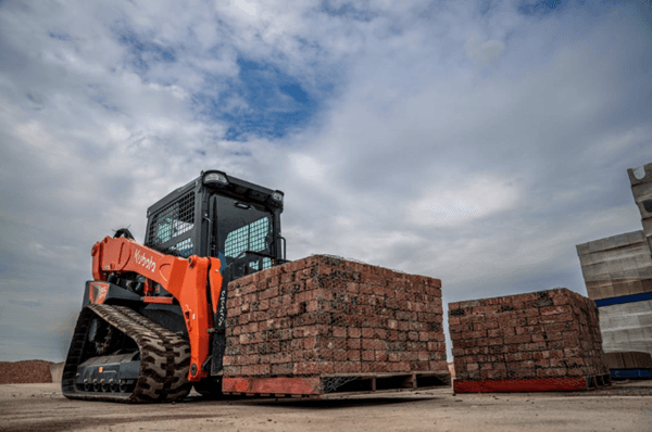 Close-up of track loader moving pallet of bricks